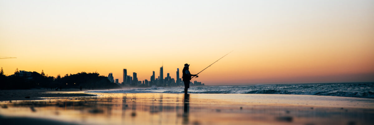 View of the coastline at City of Gold Coast, from the beach at sunrise with the silhouette of a fisherman at the front of the image.